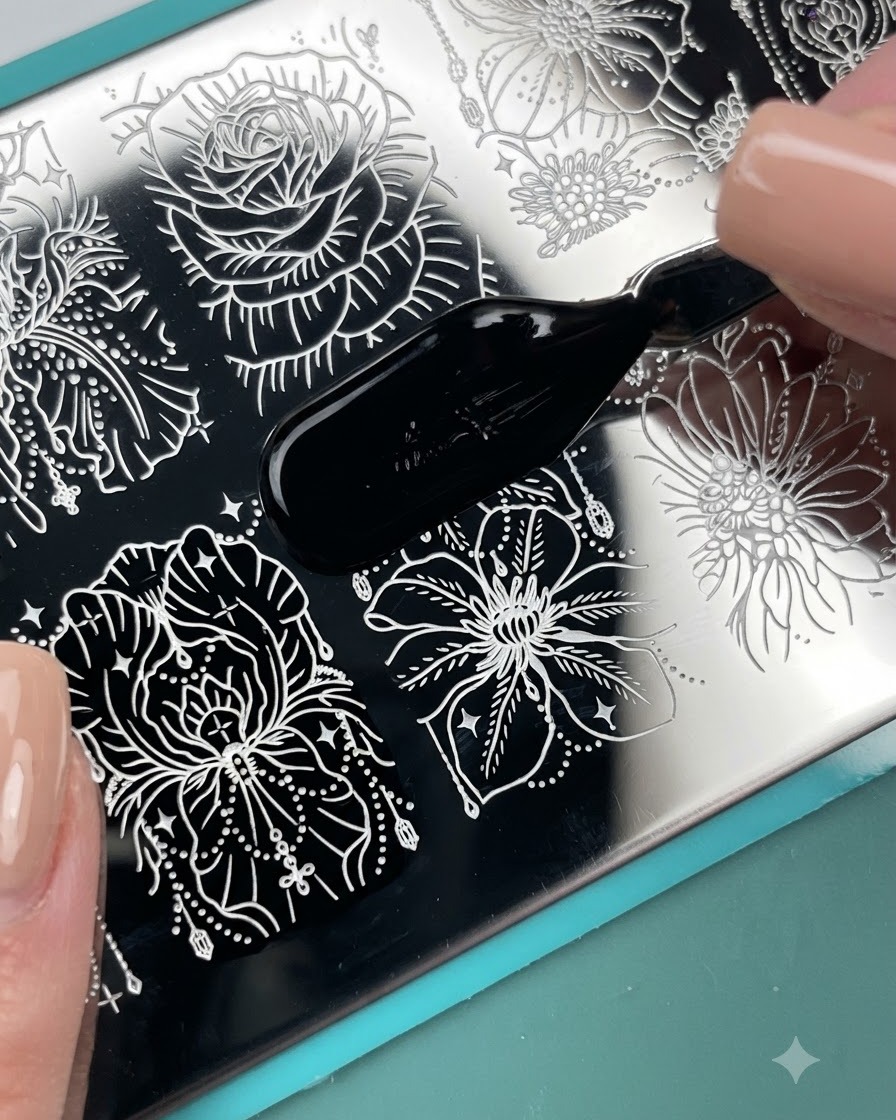 Un applicateur pinceau appliquant du vernis destampage noir sur un motif floral gravé sur une plaque destampage en métal.