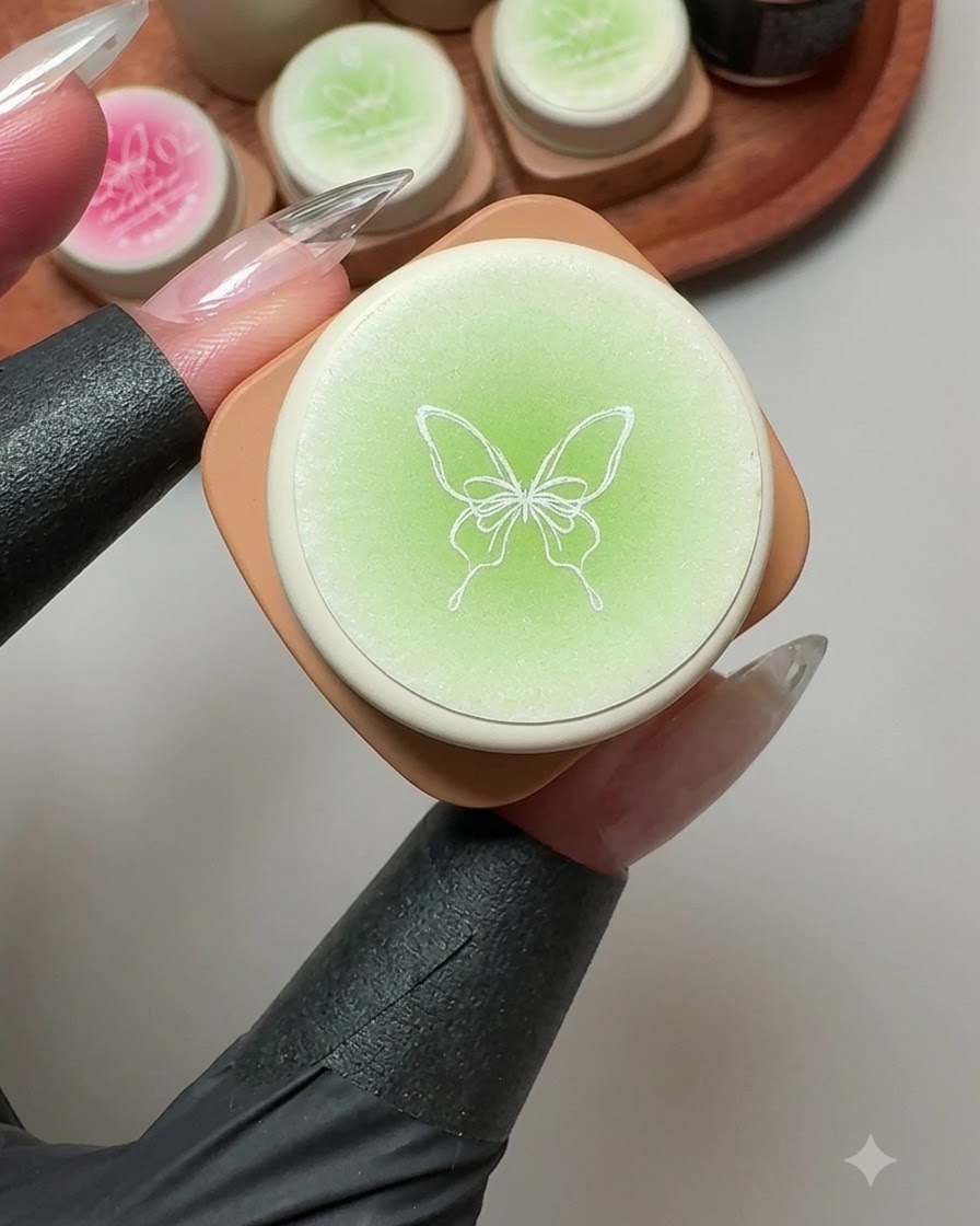 Un pot de gel solide présentant une illustration de papillon sur le couvercle, entouré de pots de gel vert et rose.