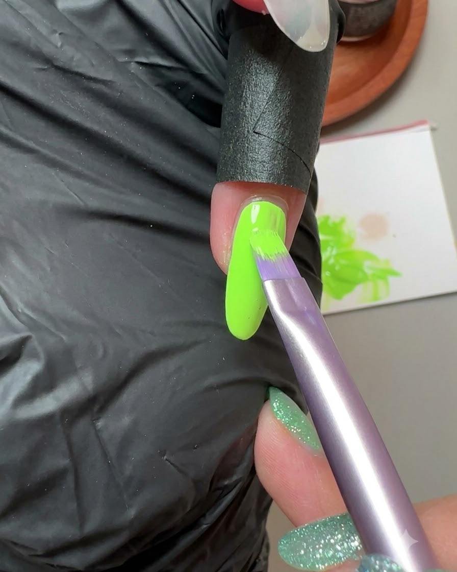 Un pinceau appliquant du gel solide vert fluorescent sur longle du petit doigt.