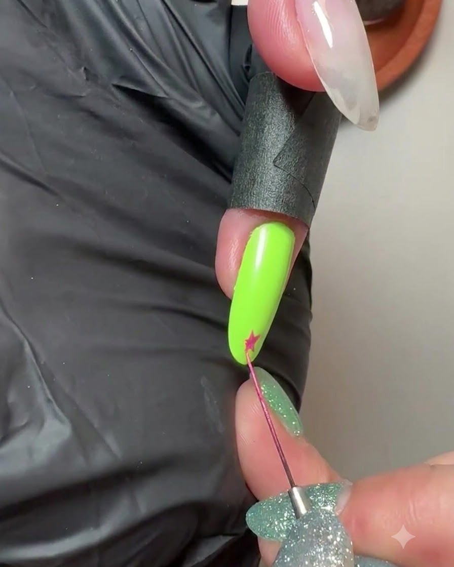 Un pinceau liner fin dessinant une petite étoile rose sur le bout dun ongle manucuré vert néon.