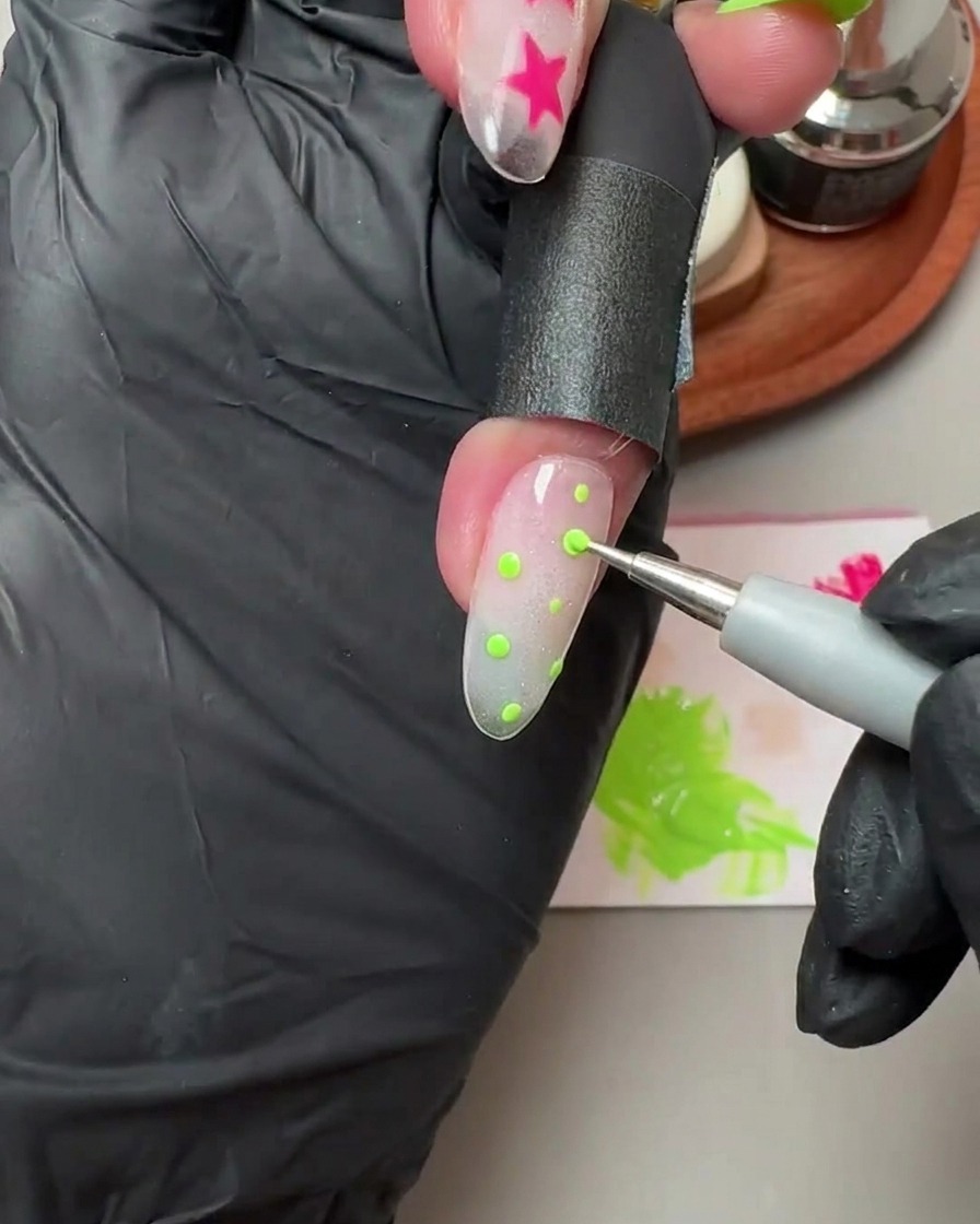 Un outil à punte placer de petits pois verts sur un ongle en gel pailleté et cat-eye translucide.