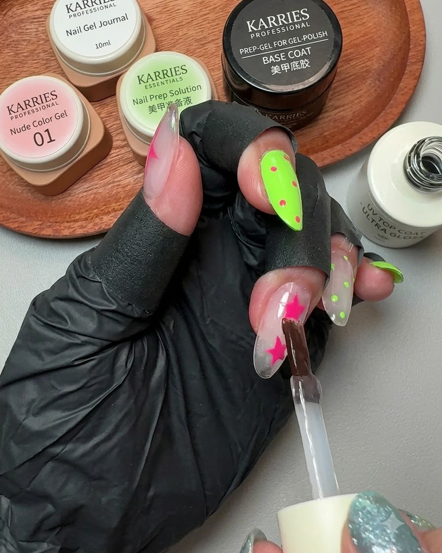 Un pinceau appliquant un top coat brillant sur un ongle décoré avec des étoiles roses et des pois.