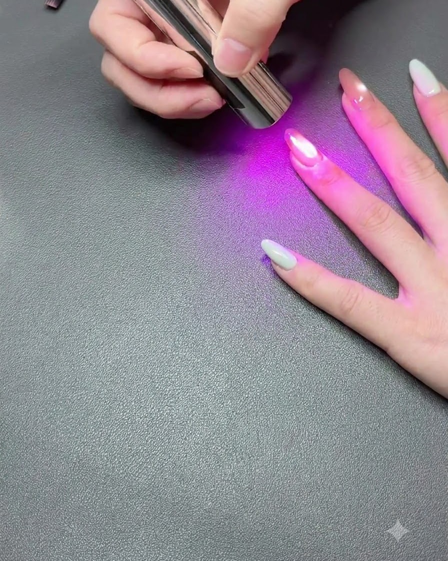 Une main reposant sur une surface sombre tandis quune lampe UV portable polymérise le vernis gel cat-eye.