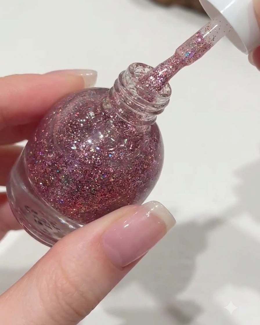 Une main dévissant le bouchon blanc dun flacon de vernis à ongles Orange, extrayant un pinceau dégoulinant de gel pailleté rose.