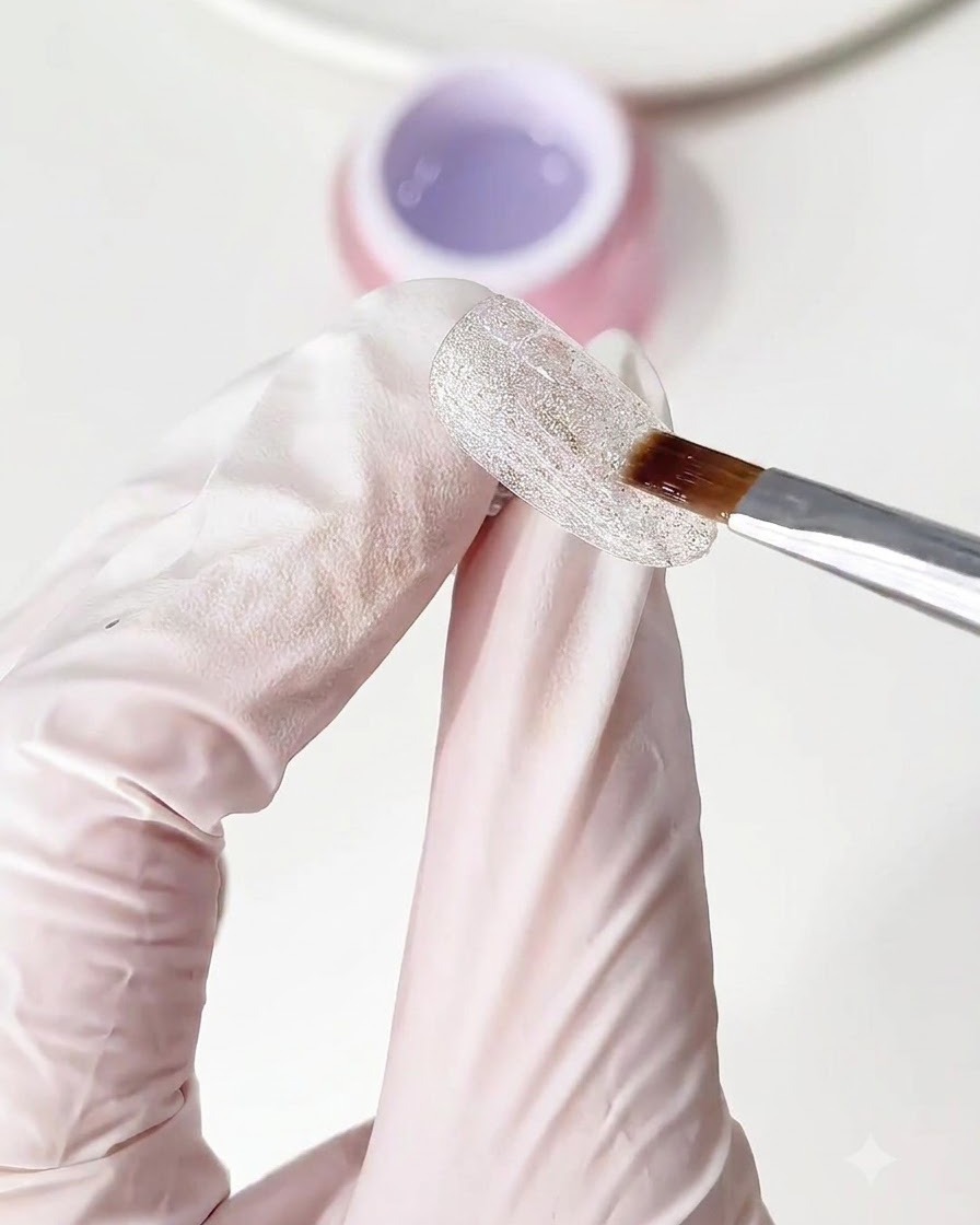 Un pinceau appliquant une couche transparente de gel de base sur la base dongle scintillante en diamant écrasé.