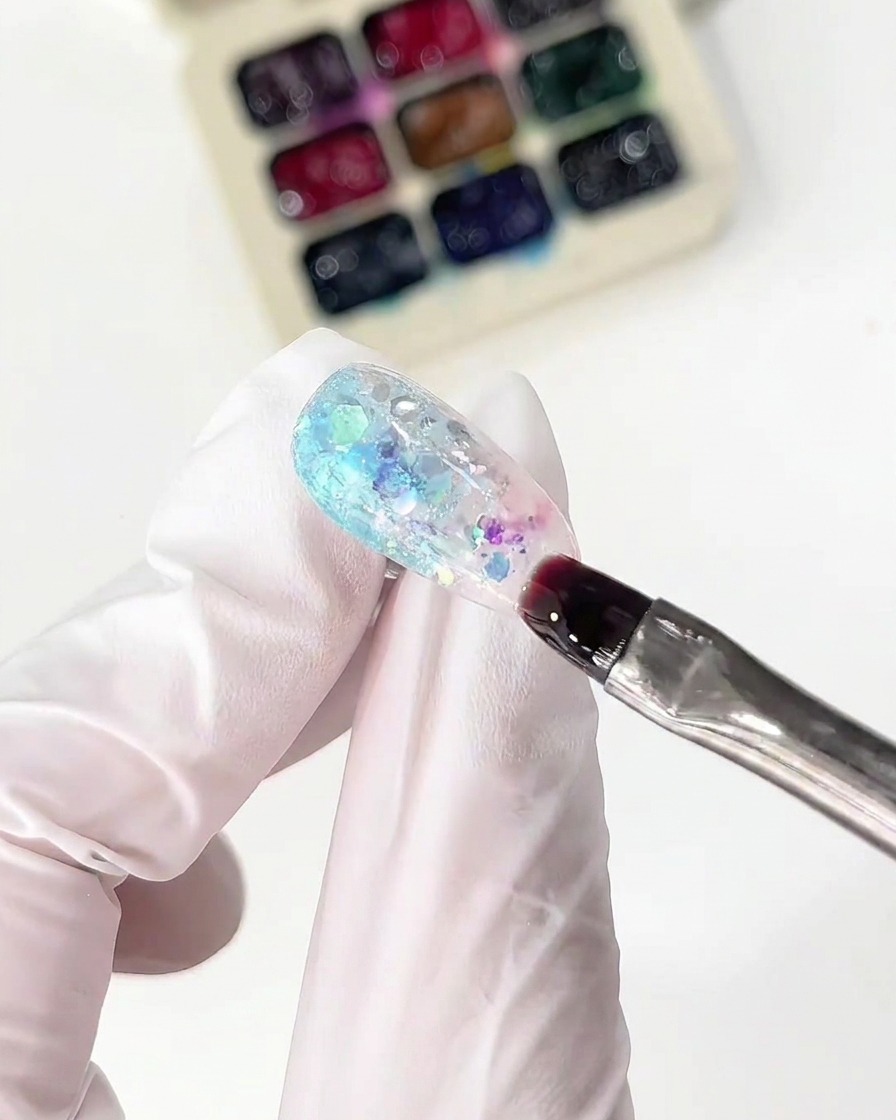 Un pinceau fin appliquant du gel verre rose à côté de la section bleue sur un ongle.