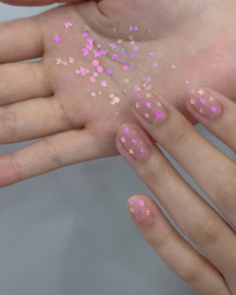 Un pinceau de manucure appliquant une fine couche de vernis gel nude translucide sur un ongle naturel.