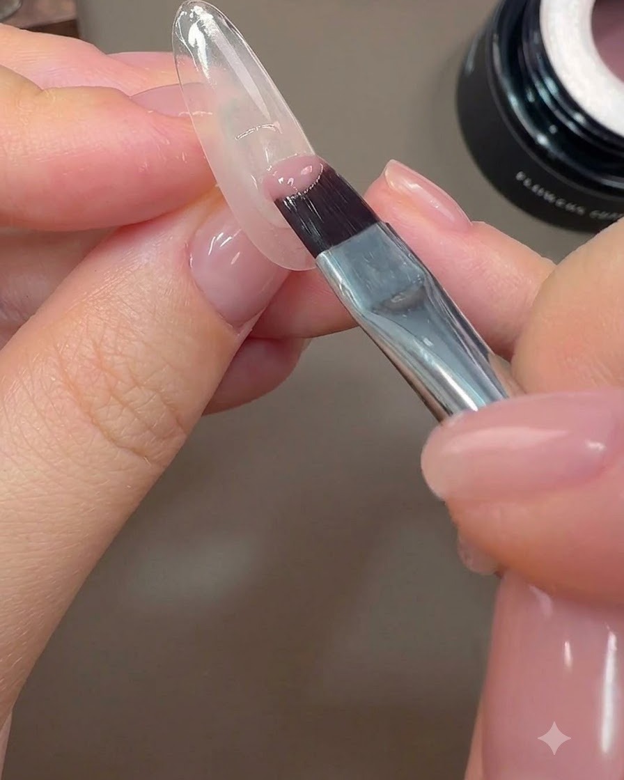 Un pinceau à ongles appliquant une demi-couverture de gel couleur rose nude sur le bord postérieur dun ongle.