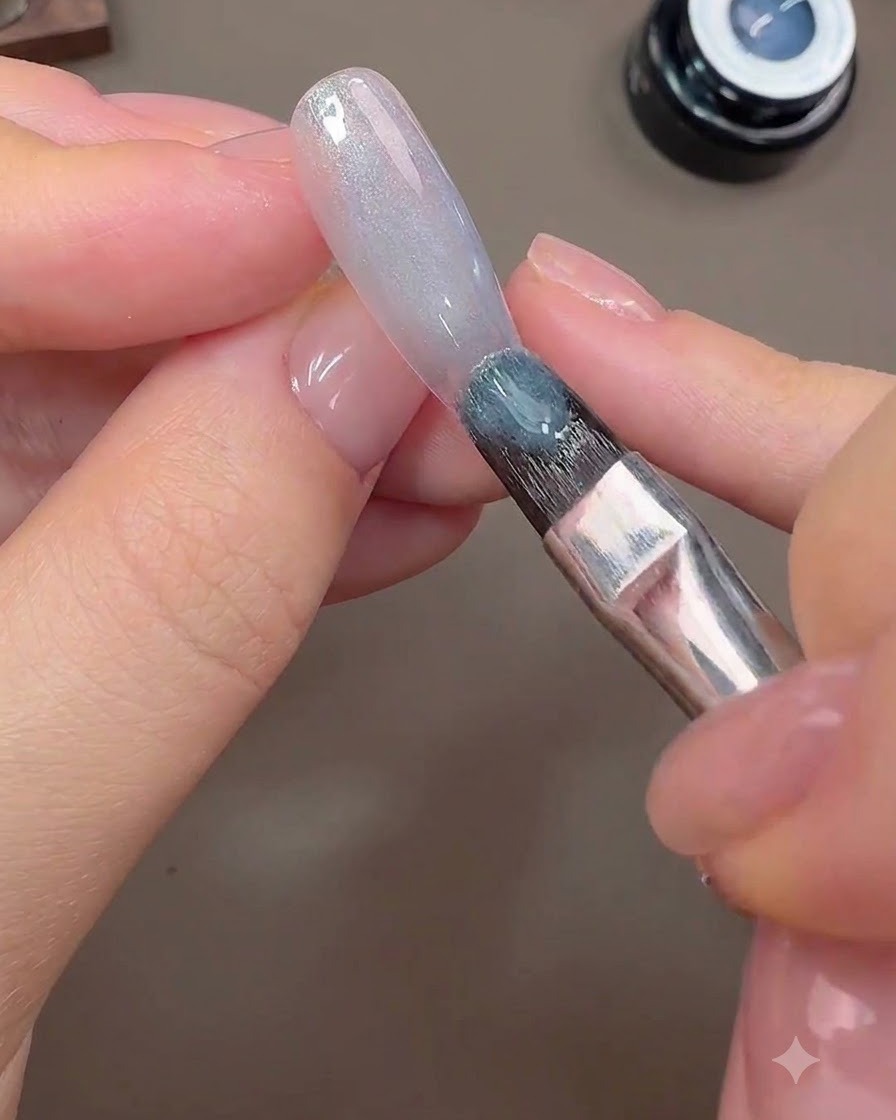 Un pinceau appliquant du gel cat-eye gris-bleu sur la surface de longle pour former larrière-plan galactique.