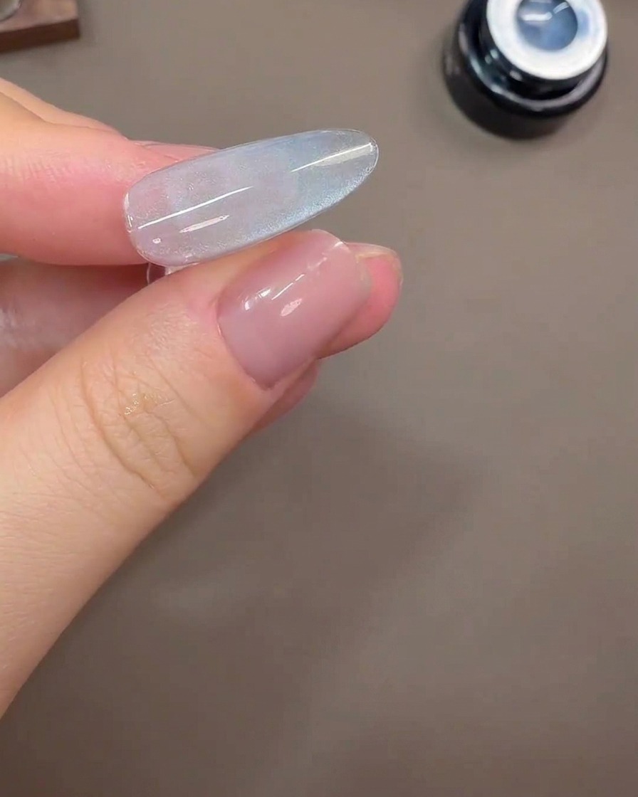 Un ongle montrant un large reflet lumineux cat-eye sur un fond en gel gris-bleu.