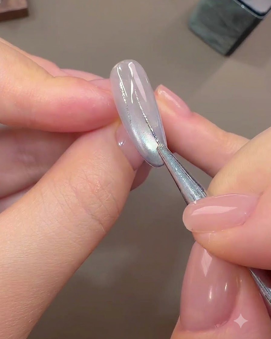 Un pinceau fin de nail art dessinant de fines lignes abstraites avec du gel foil argenté sur un ongle de base clair catalysé.