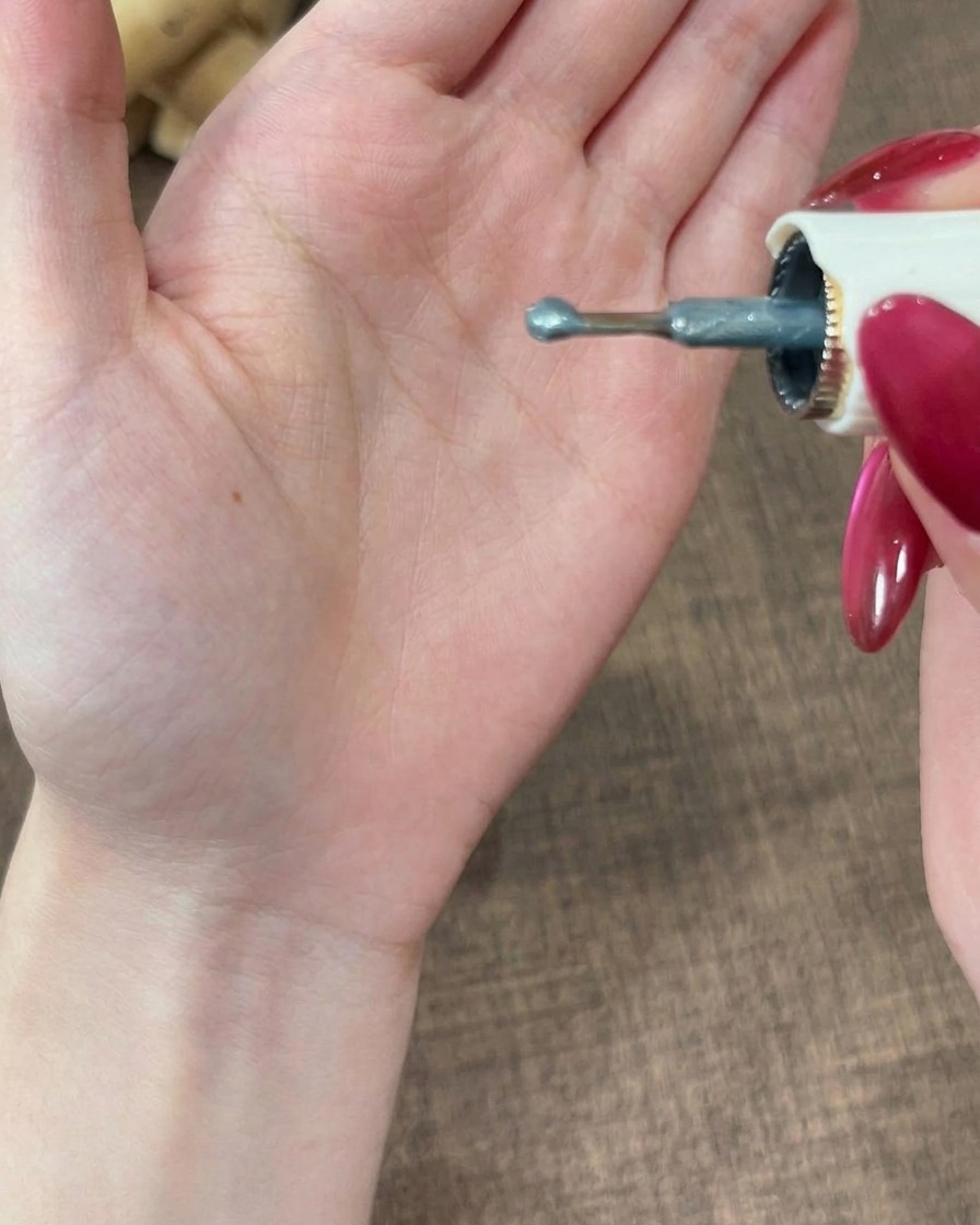 Une vue rapprochée de la pointe dun pinceau tenant une petite perle arrondie de vernis gel grisâtre.