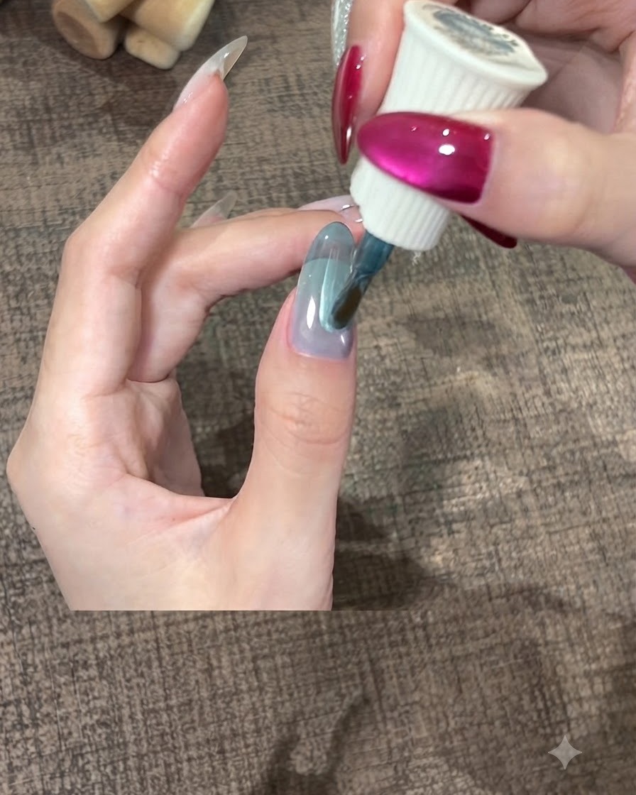 Un pinceau étalant une épaisse couche de vernis gel teal en douceur sur un ongle de pouce.