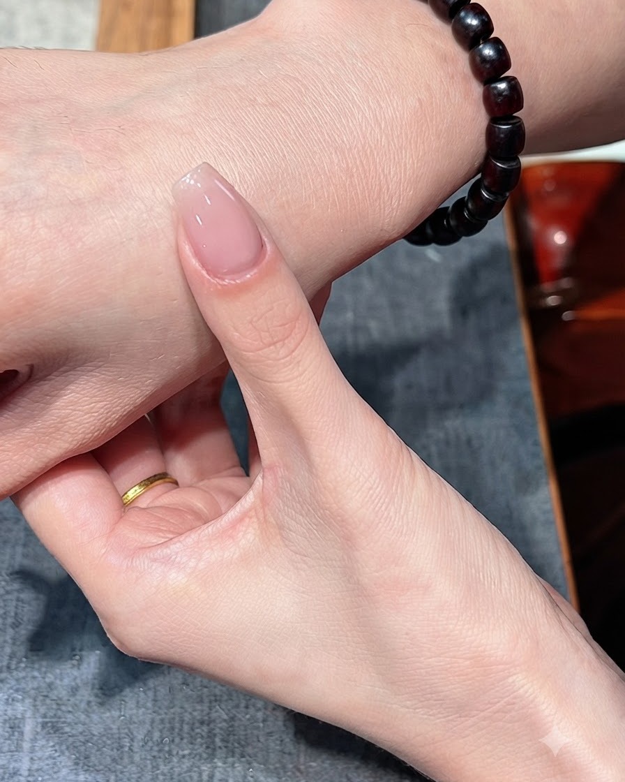 Un ongle avec une seule couche de vernis nude tenu contre le dos de la main.