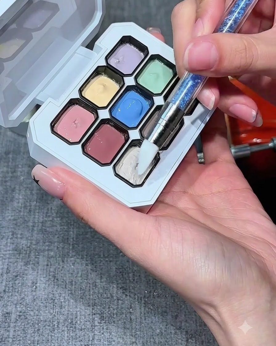Un pinceau à ongles en silicone trempant dans un puit de gel blanc laiteux sur une palette multicolore.