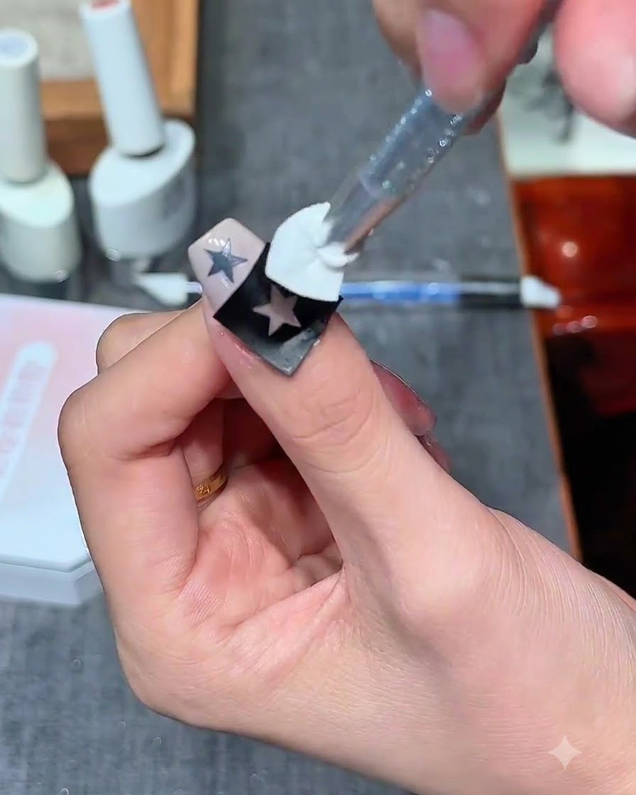 Un tampon éponge appliquant du gel blanc laiteux par-dessus un autocollant détoile creuse sur un ongle.