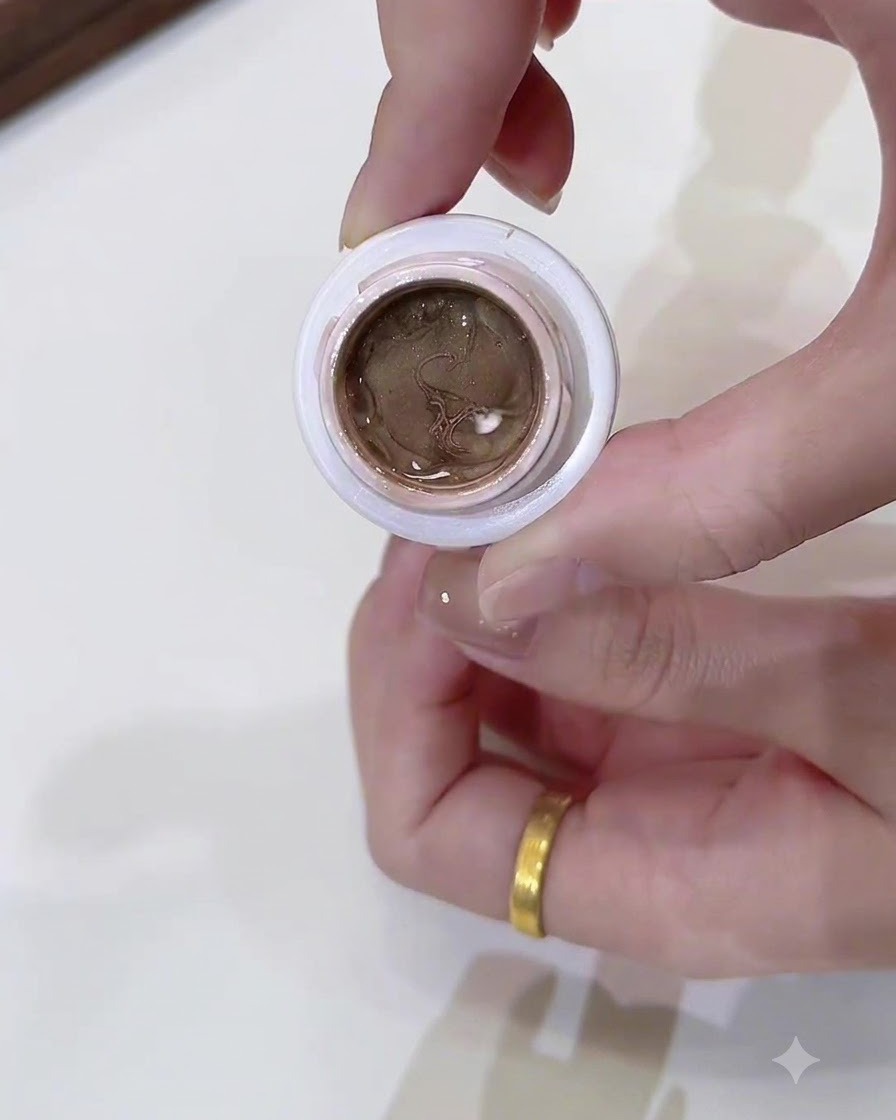 Gros plan dun petit pot ouvert rempli de gel cat-eye or champagne foncé tenu par une main.