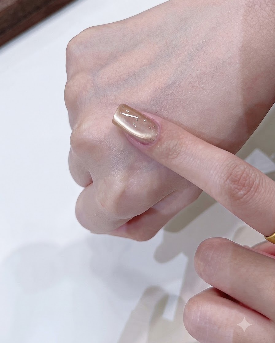 Un outil aimanté façonnant un reflet lumineux doux unilatéral sur un ongle cat-eye or champagne.