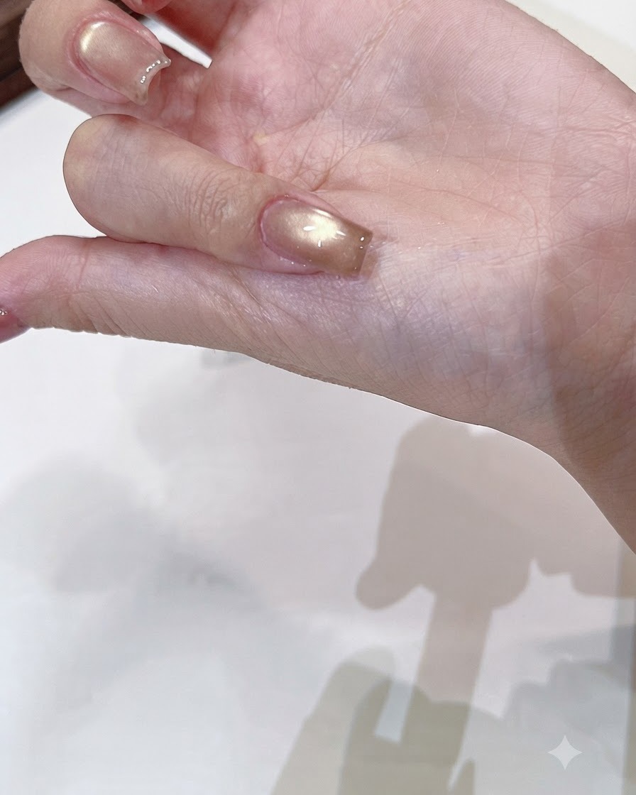 Un pinceau appliquant un top coat transparent et brillant sur un ongle cat-eye or champagne catalysé.