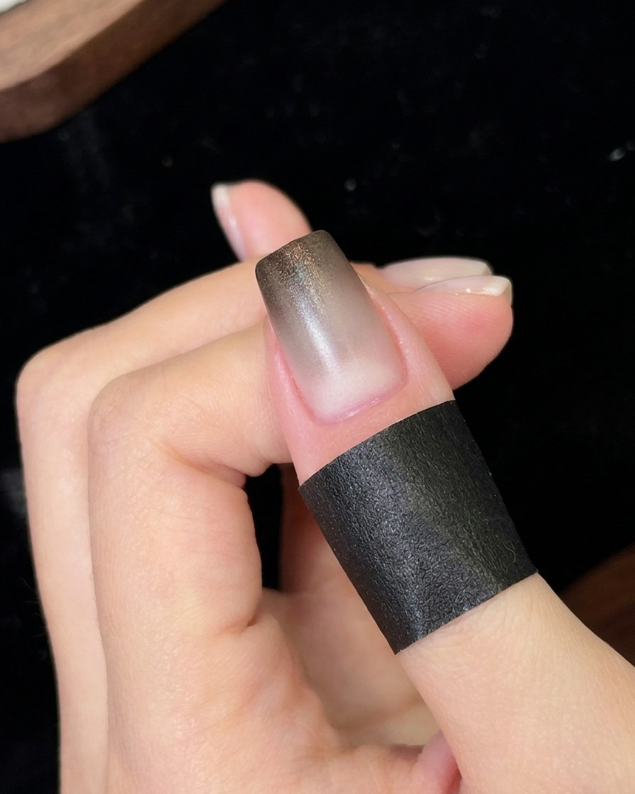 Un ongle positionné sous une petite lampe UV/LED portable catalysant la nouvelle couche de dégradé noir appliquée.