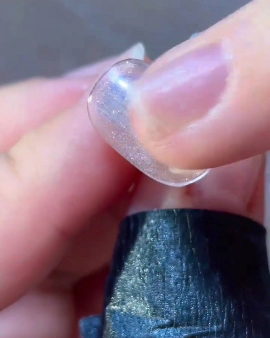 Un pinceau liner fin appliquant des détails en gel rose autour dun motif détoile sur un ongle.