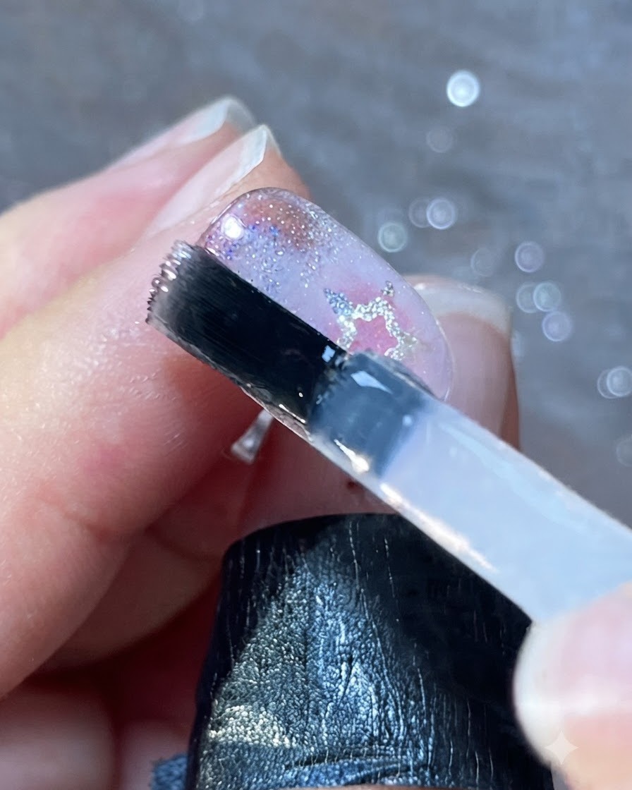Un pinceau à ongles appliquant une couche lisse de finition transparente sur des ongles décorés.