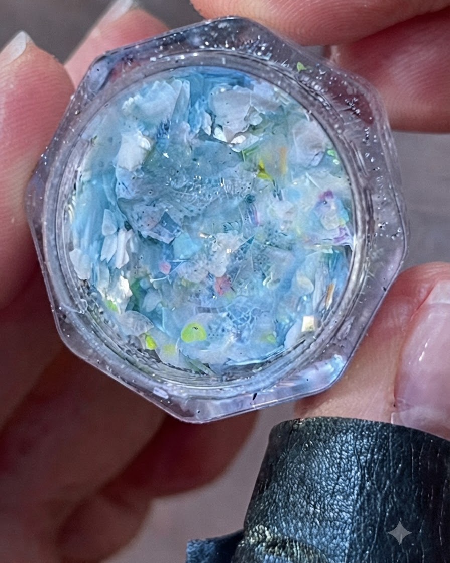 Gros plan dun pot ouvert rempli de flocons et de paillettes irisés bleus et blancs.