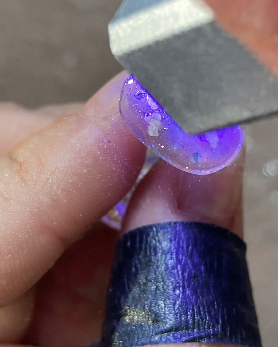 Une main sous une lampe à ongles UV/LED violette catalysant un design dongle décoré.