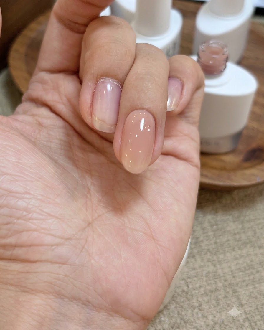 Vue rapprochée dune main avec une couche de gel de base transparent humide et brillant appliquée sur longle rose nude.