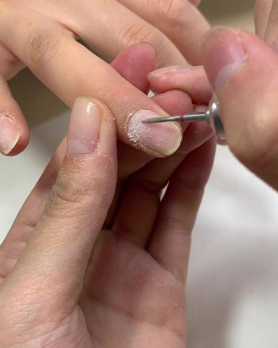 Un pinceau appliquant une couche transparente de base en gel sur un ongle naturel.