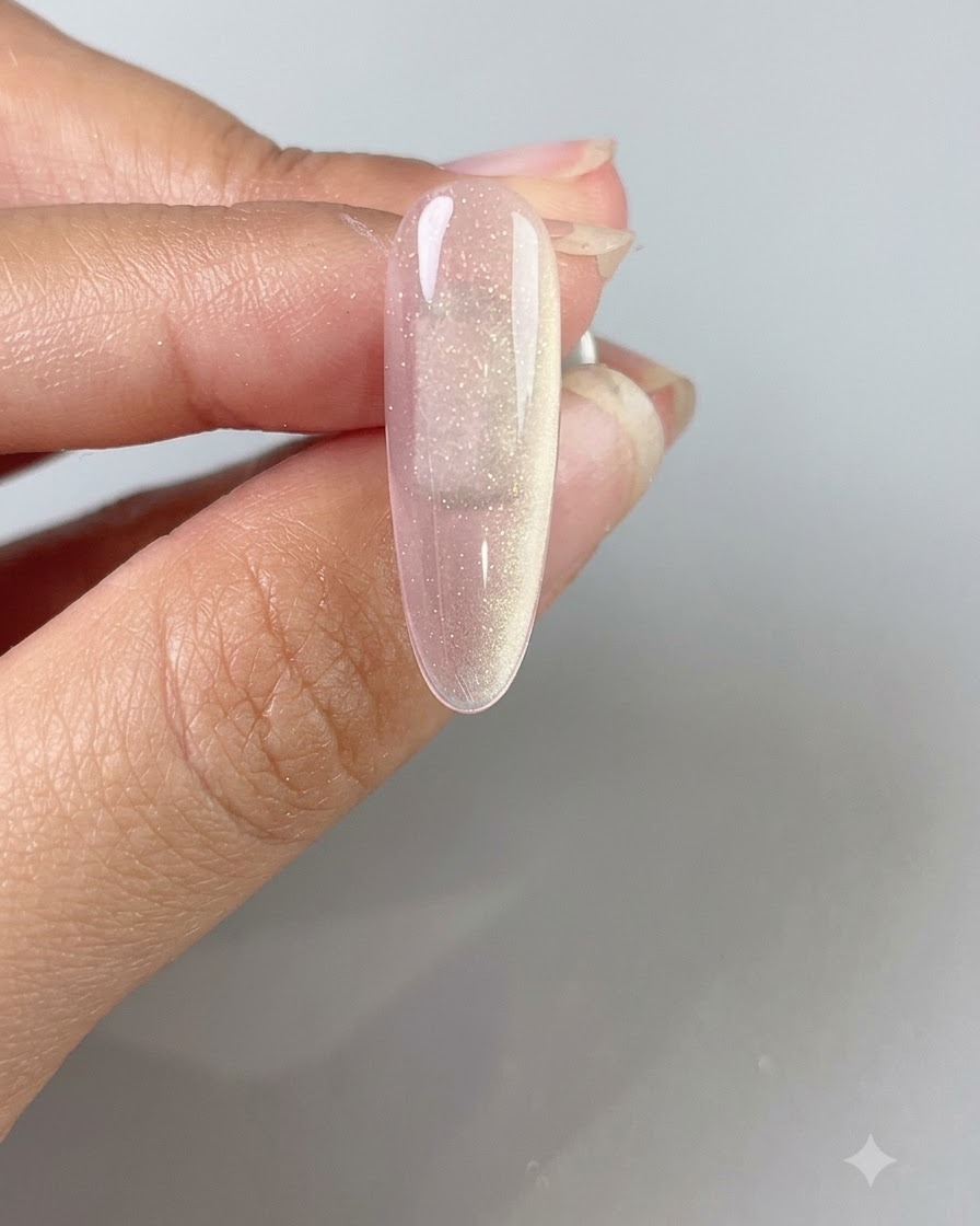 Une main tenant un bâtonnet magnétique au-dessus dun ongle en gel cat-eye rose translucide pour créer un large faisceau lumineux.