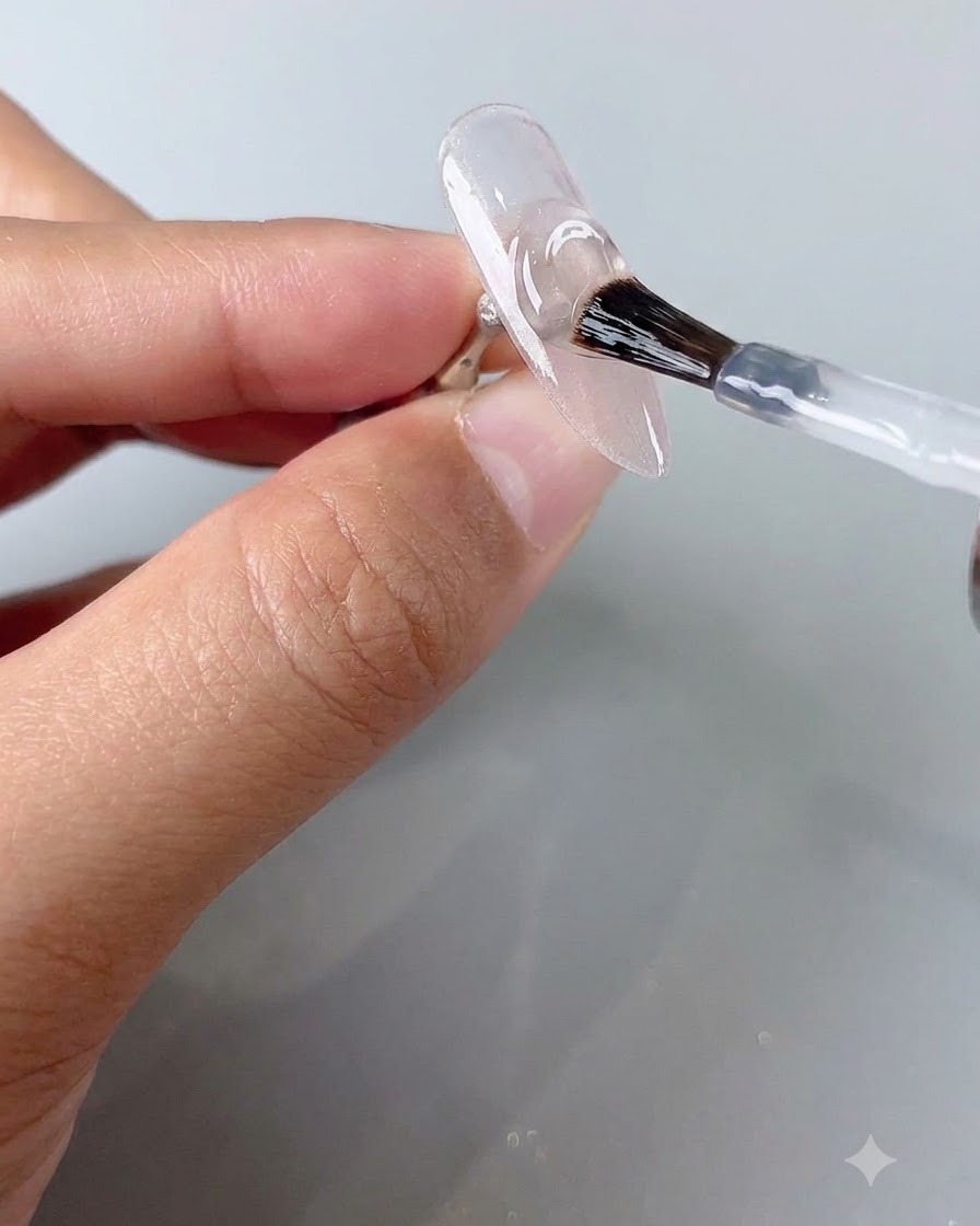 Un pinceau à ongle appliquant une couche de finition transparente sur un ongle cat-eye catalysé.