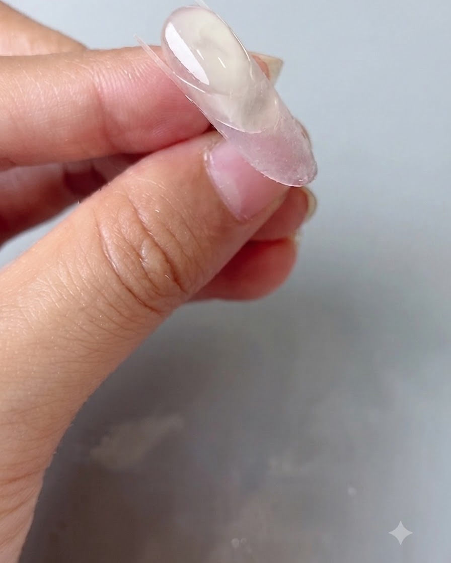 Un outil de modelage en silicone pressant un sticker guide transparent sur un ongle ovale.