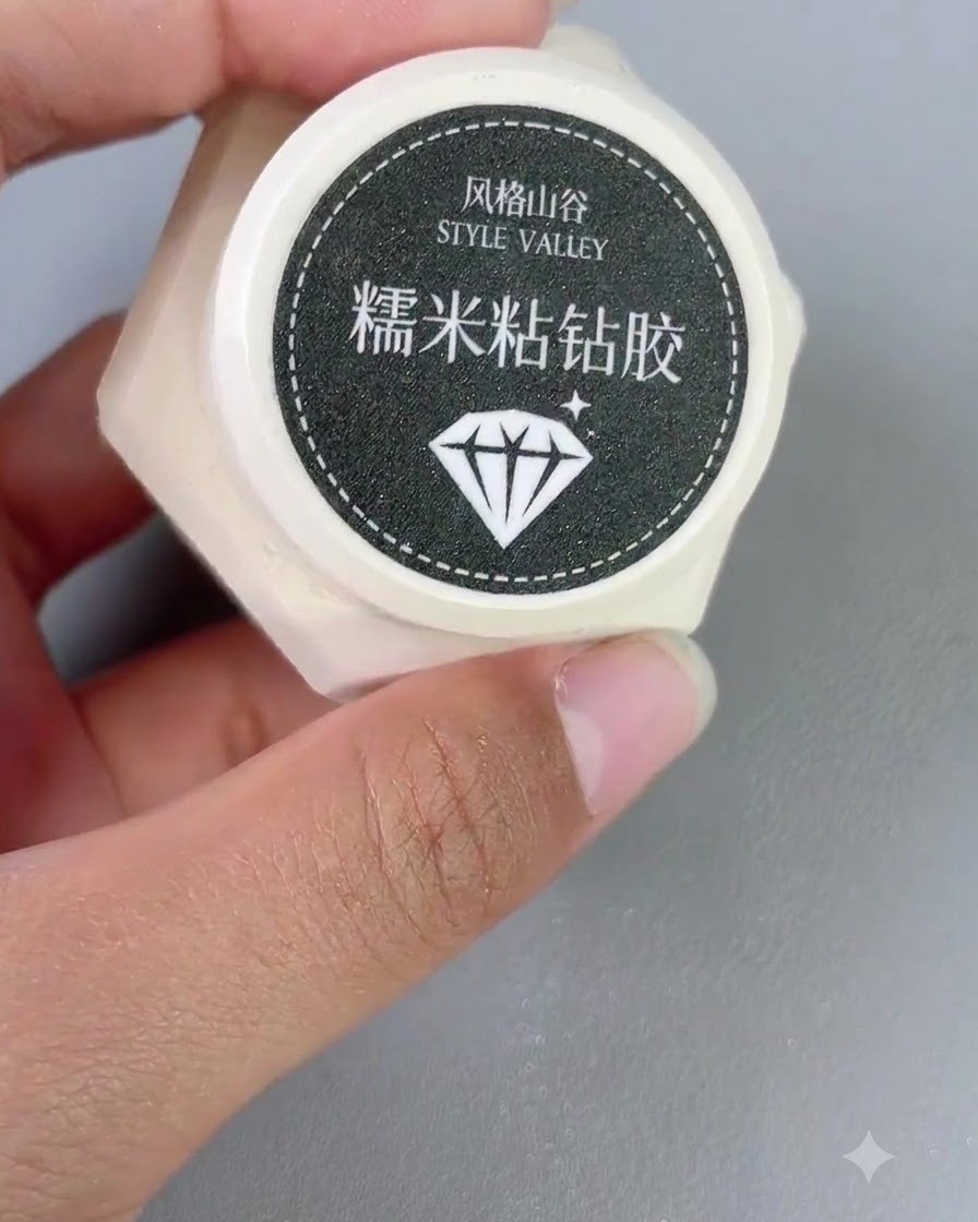 Un petit contenant de gel adhésif diamant Style Valley tenu dans une main à côté dun pinceau à ongle.