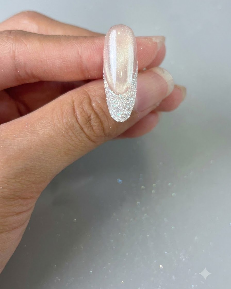 Une main tenant un ongle fini avec une French tip pailletée, prête pour la catalysation finale.