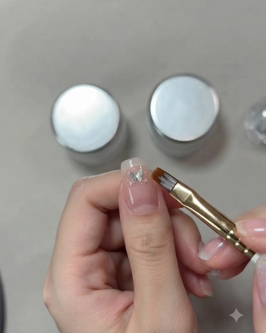 Gros plan détaillé de la main dun prothésiste ongulaire utilisant un pinceau fin pour positionner un petit sequin papillon argenté sur un ongle œil de chat rose.