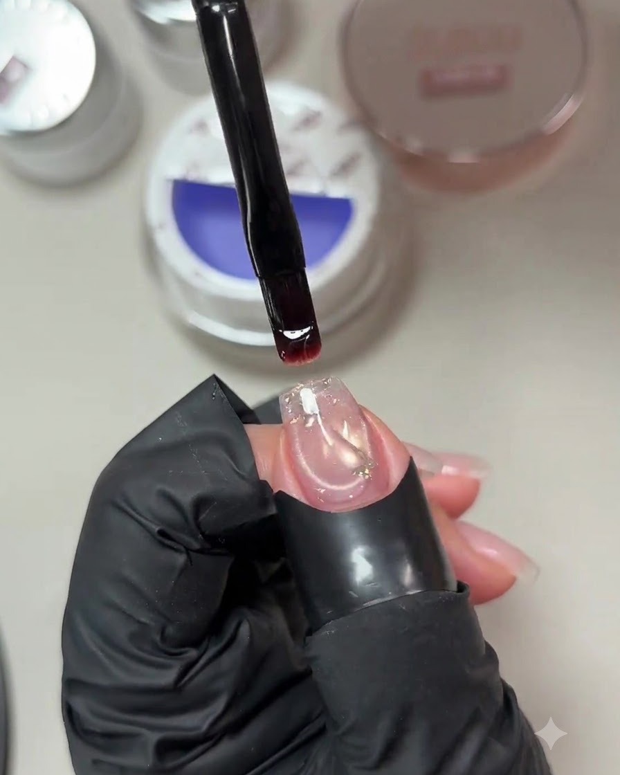 Un pinceau retenant une goutte de gel de construction bleu violacé pâle au-dessus dun ongle préparé avec un sequin incrusté.