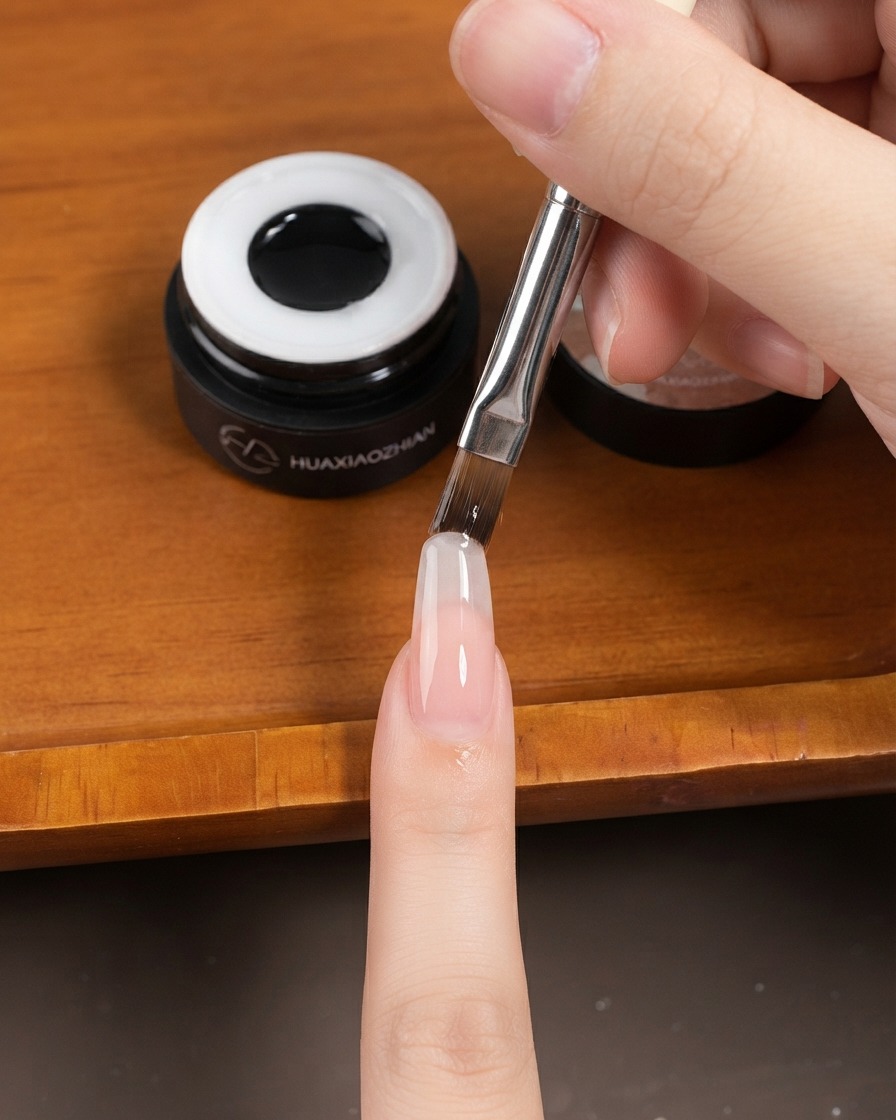 Un pinceau plat à gel appliquant une fine couche de gel sur un ongle long en forme damande.