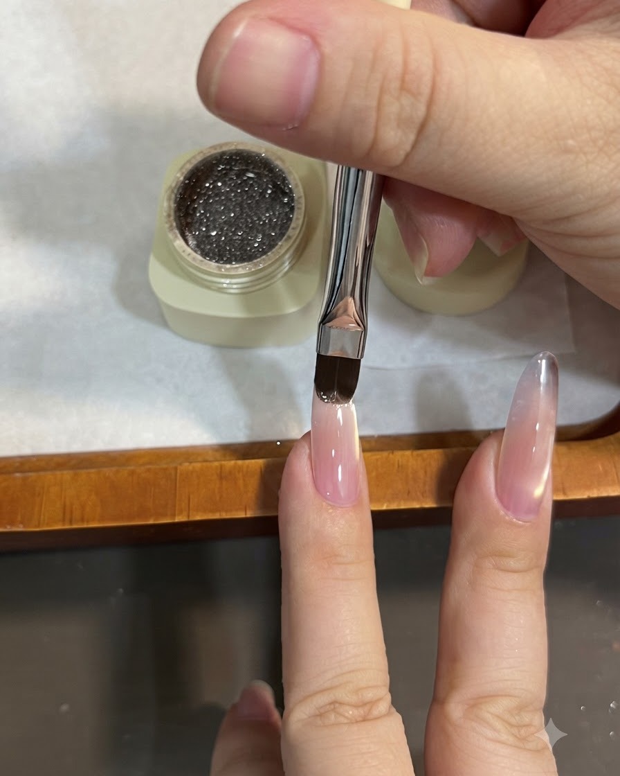 Un pinceau plat appliquant du gel pailleté marron sur le bord libre dun ongle en amande, en effectuant un balayage vers le bas pour créer un effet ombré.