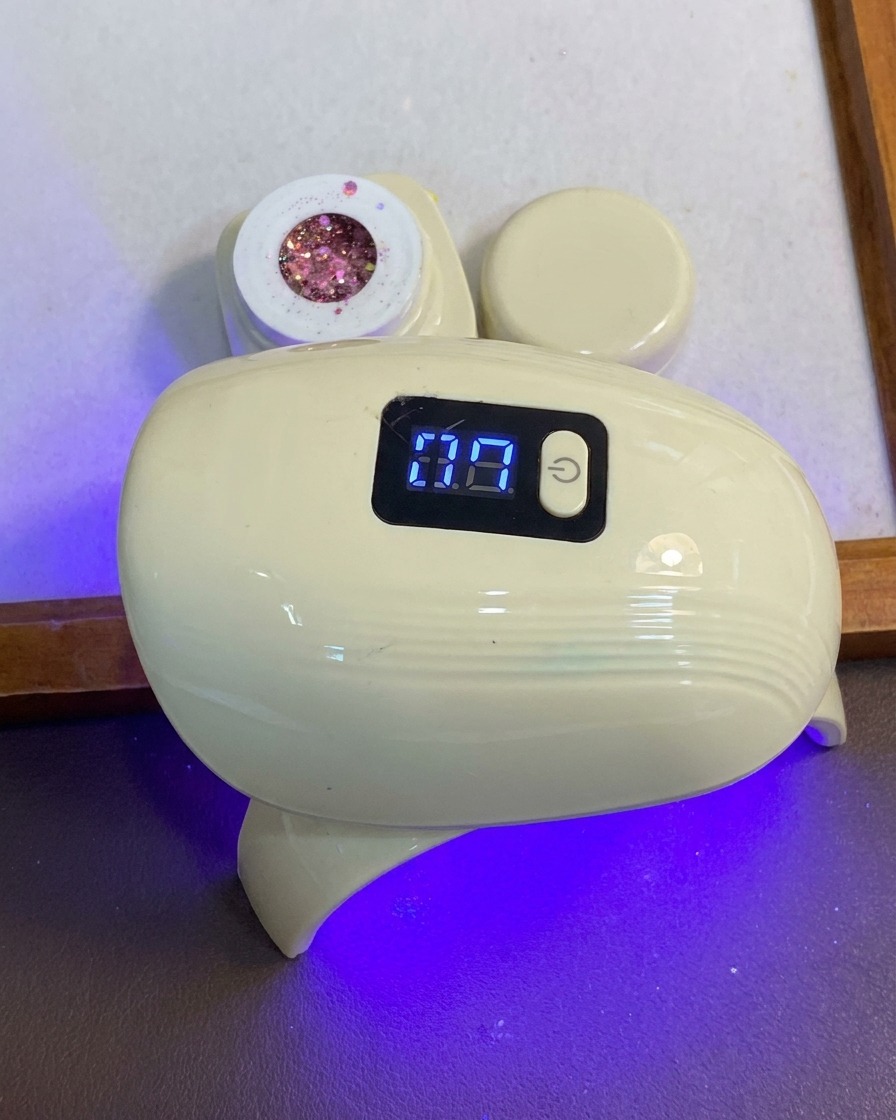 Une main plaçant ses doigts sous une lampe de catalysation LED compacte bleue et blanche.