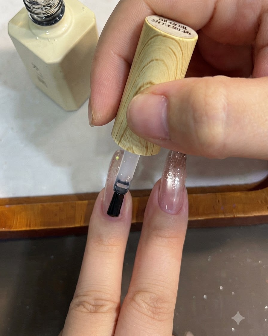Un pinceau appliquant un top coat transparent sur un design dongles en dégradé de paillettes.