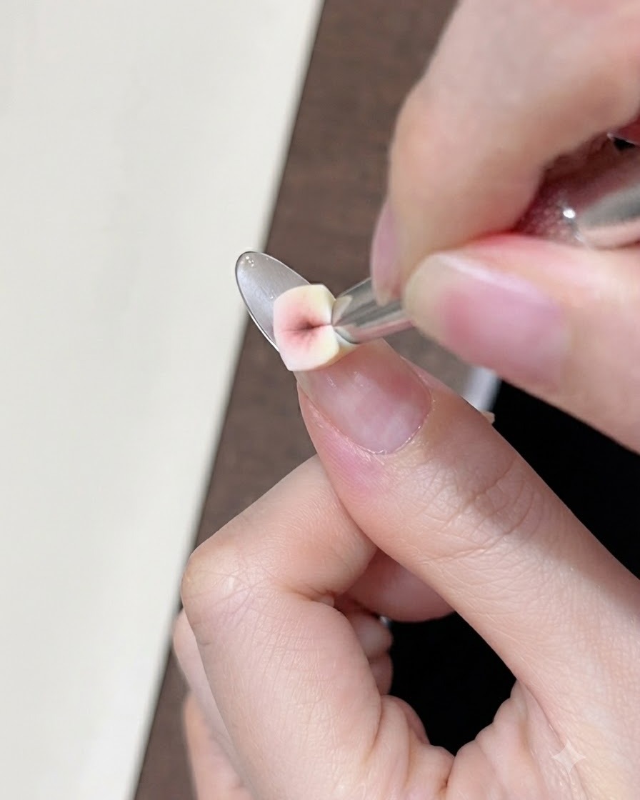 Gros plan dune petite éponge en coin appliquant du gel correcteur nude sur longle naturel près de la ligne du sourire.