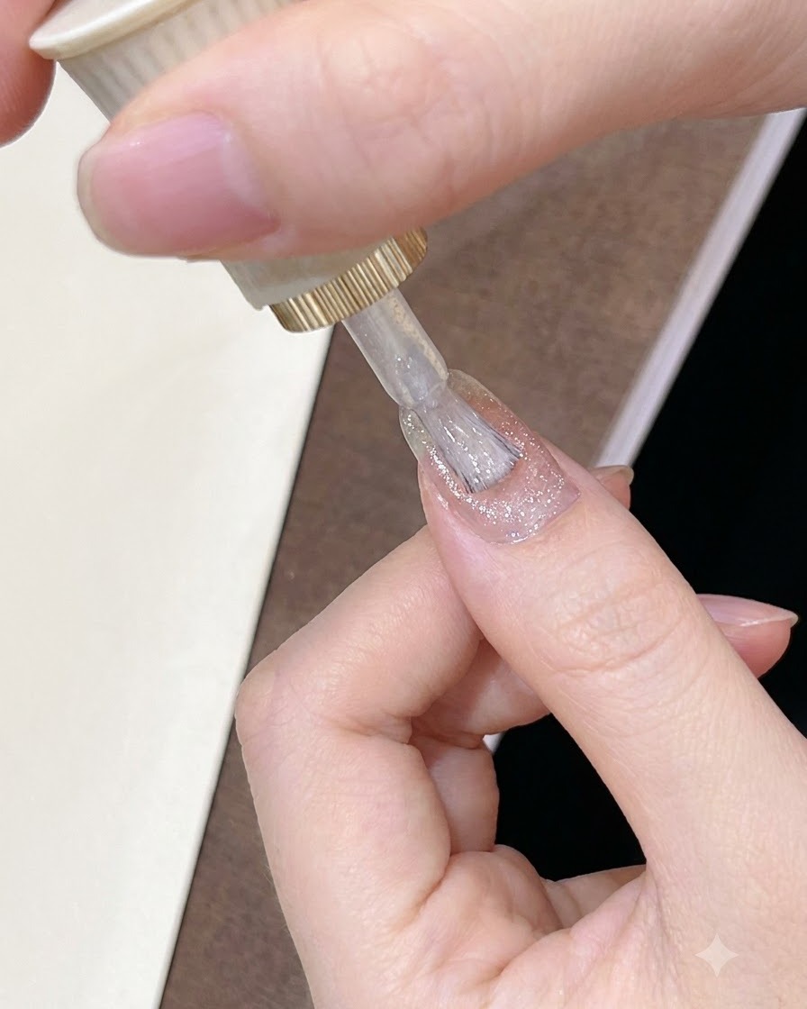 Un pinceau appliquant un vernis gel rose-brun diaphane et lumineux sur la surface dun ongle manucuré.