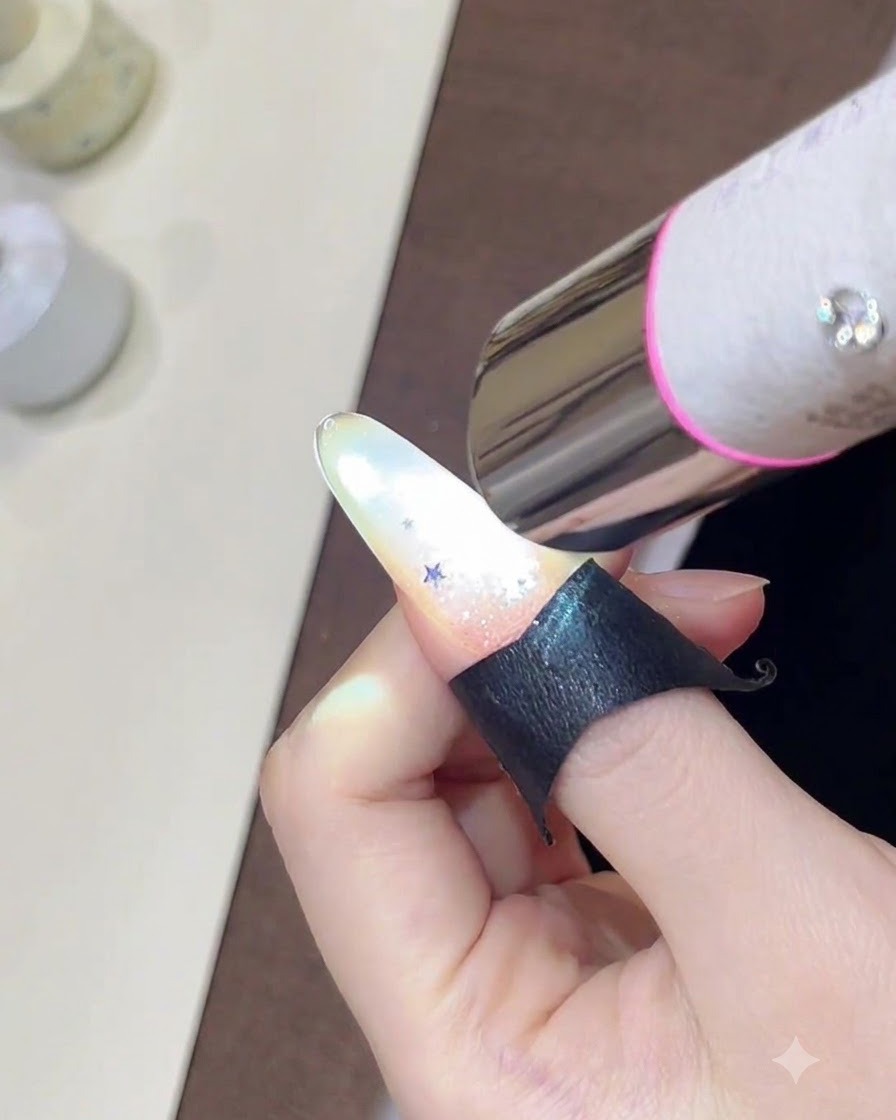 Une main tenant une mini lampe UV au-dessus dun ongle décoré dun dégradé de paillettes scintillantes et de petits sequins détoiles.
