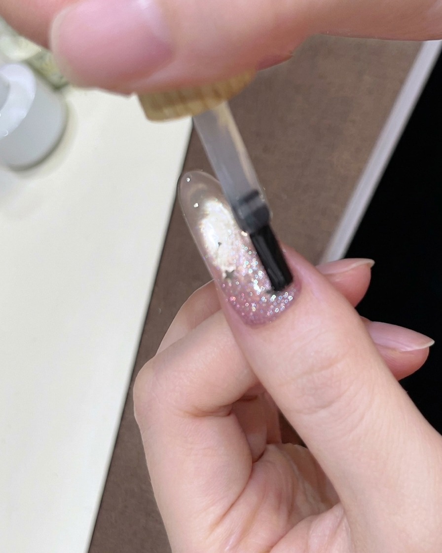 Un pinceau appliquant un top coat transparent et brillant sur longle décoré en dégradé.
