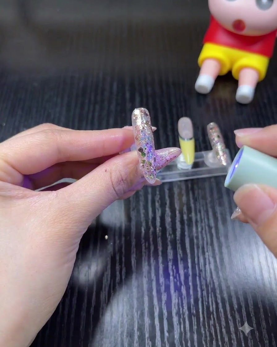 Une main tenant une mini lampe UV/LED portable au-dessus dun ongle pailleté pour catalyser le gel.