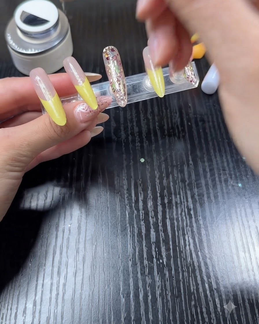 Un pinceau de vernis appliquant un top coat transparent sur un ongle doté dune French manucure jaune vif.