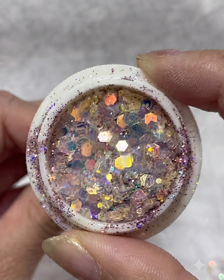 Un pot rempli de flocons de paillettes irisées multicolores, de sequins et de petites étoiles tenu entre les doigts.