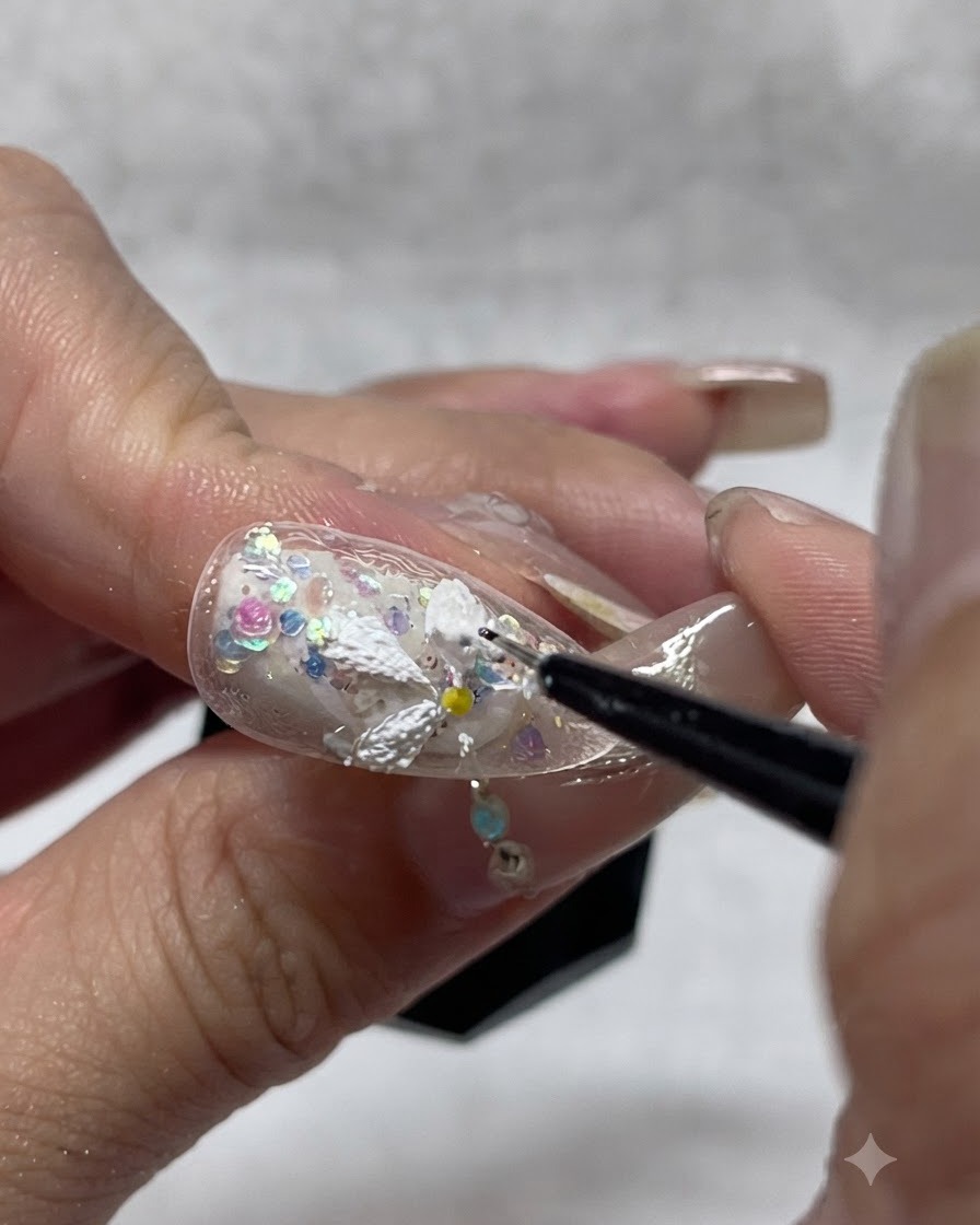 Une prothésiste ongulaire ajoutant du gel texturé blanc supplémentaire sur les pétales de marguerite peints pour accentuer la profondeur et lopacité 3D.