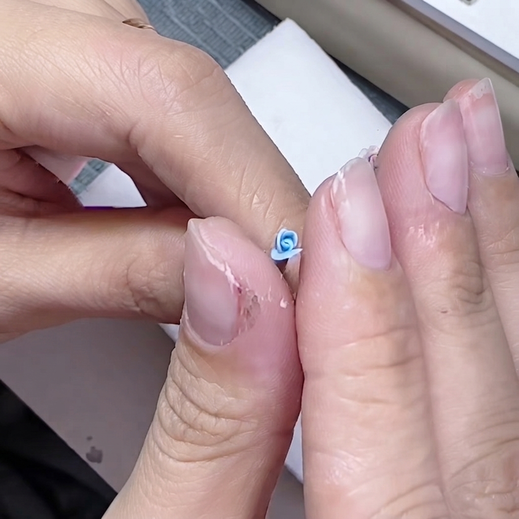 Doigts pinçant délicatement la base dun petit pétale bleu autour dun cœur de rose sculpté.
